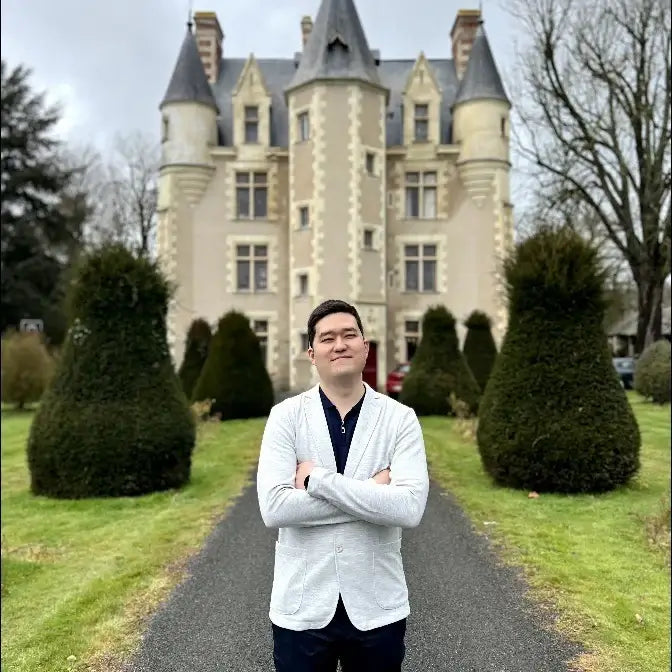 Daulet Dauysbekov, cofounder and lead developer of the ShopiCraft agency building Shopify stores and solutions in a white suit jacket and a castle in the background.